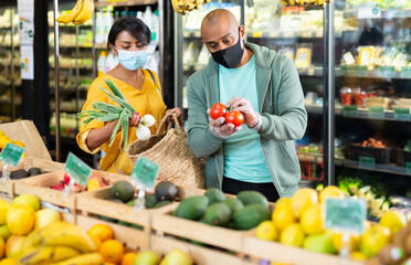 Obraz premium Married couple in protective mask choosing ripe tomatoes at grocery store
