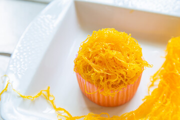 Top view a mamon cup cake with golden thread topping on a a white wooden table.
