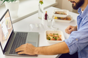 Fototapeta na wymiar Man signing up for food delivery website using laptop while having lunch break in the office