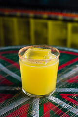 An orange cocktail in a rocks glass with a big ice cube and spicy rim on the glass