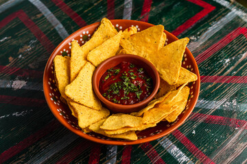 A plate of nachos with spicy salsa dip on a wooden table