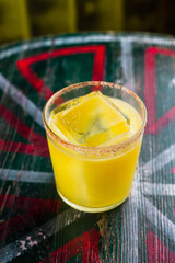An orange cocktail in a rocks glass with a big ice cube and spicy rim on the glass