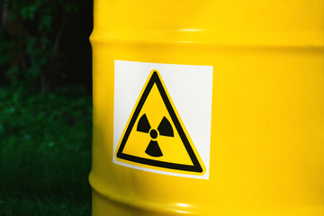 ..The nuclear sign on a yellow metal barrel on the green grass. Radiation hazard symbol sign....