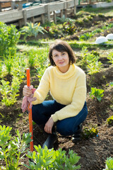 Young positive woman working with sprouts in vegetable garden