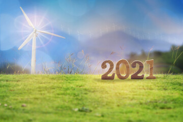 New year 2021 on grasses with wind turbines on mountain background. Renewable clean energy...