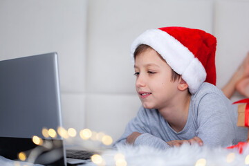 Cute little boy child in red santa hat at homelooking at laptop computer screen watching online...