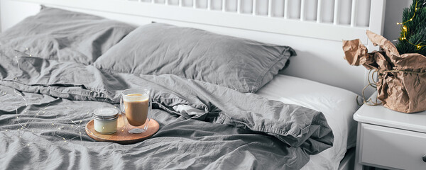 Wooden tray with coffee glass and candle on bed in bedroom. Light scandinavian interior. Morning...