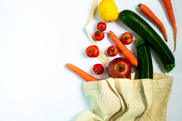 Flat lay of a reusable bag with organic groceries on a white background. Apples, zucchini, carrots, lemon and tomatoes