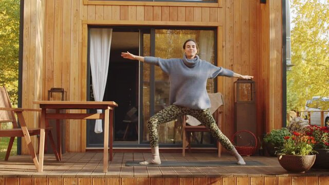 Young Caucasian woman practicing yoga outdoors on terrace of wooden country house on beautiful autumn day