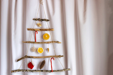 Hand made eco friendly christmas tree out of wooden sticks, oranges, cones and lights. Сhristmas tree in scandinavian style.