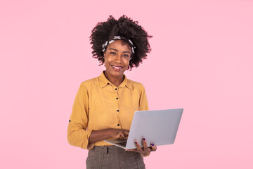 African american woman holding laptop smiling and looking at camera. Young beautiful woman feeling happy, standing isolated over pink background
