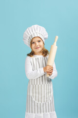 cute little girl in chef hat and apron holding rolling pin on blue background. child dreams of becoming a chef