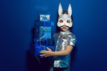 Christmas baby boy in hare mask with gift in Studio on blue wall background