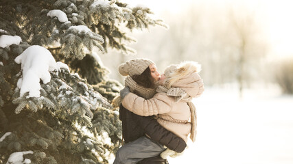 Little girl in beige fur coat kissing and hugging her mother on a sunny frosty day. Happy family...