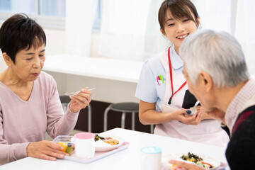 Obraz na płótnie Canvas 食事中の高齢の入居者たちと楽しく会話している介護施設の女性職員