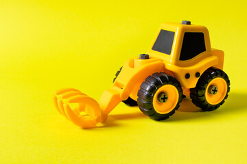 Fototapeta na wymiar Children's construction machine lumber loader on a yellow background. Tractor for the boy and photo for the toy store with a place for text copy space