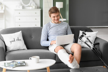 Young man with broken leg using laptop at home