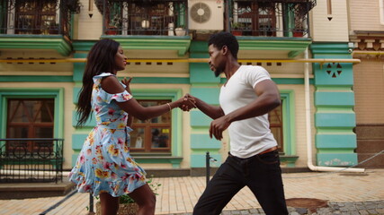 Serious afro guy controlling girl in dance in city. Couple dancing outdoors