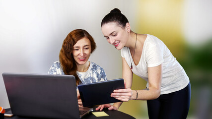 Two young smiling women in casual clothes are working or having fun near their laptop. Work from home or have fun on social media. Close-up.