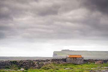 Old stone shed with red rusty roof and dry stone wall Dun Aonghasa stone fort in the background....