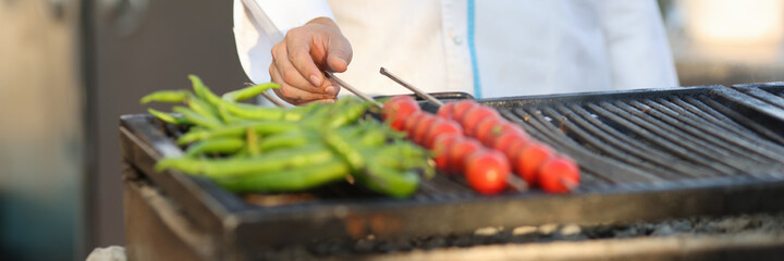 Cook prepares green peppers and tomatoes on brazier outside. Vegetarianism and cooking in hotels