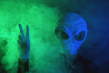 Alien is showing victory gesture on dark background.
