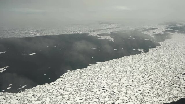 Chunks of ice on the water. Aerial view. Lots of broken ice. Low cloud. The ice is melting. Exploration of the ice situation.