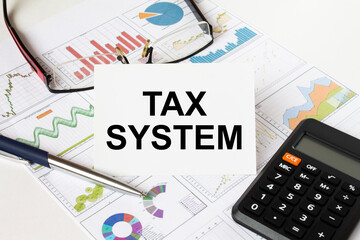 White card with text Tax System it is lies on financial charts with a calculator and eyeglasses