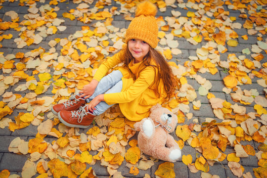 Happy little girl playing with his teddy bear toy in autumnal park