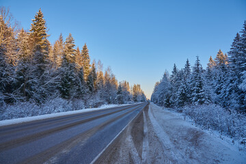 Car paved road in the middle of a snow-covered forest under a bright blue sky. Winter landscape.