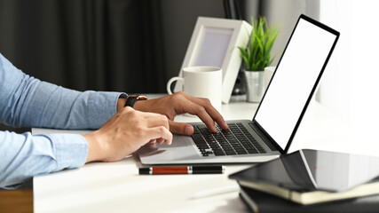 Cropped shot of young man hands typing on laptop keyboard at his comfortable workspace.