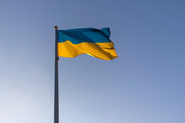 Big flag of Ukraine on a high flagpole against a clear sky.