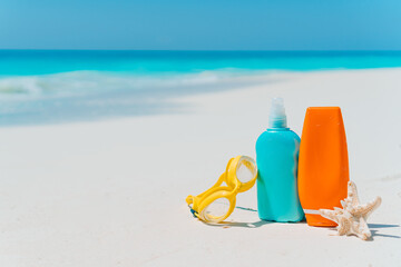 Suncream bottles, sunglasses, starfish on white sandy beach