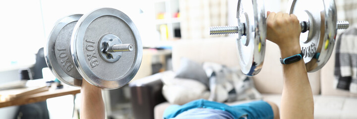 Man at home raises barbell and shakes his biceps. How to stay fit in the coronavirus pandemic...