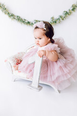 A little cute girl in a beautiful dress holds the number 1 in her hand. first birthday