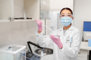 science, chemistry and people concept - young asian female scientist in mask and goggles working on vaccine over hospital or laboratory background