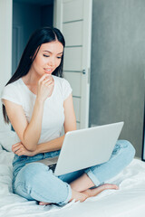 Curious lady thoughtfully looking at the screen of laptop