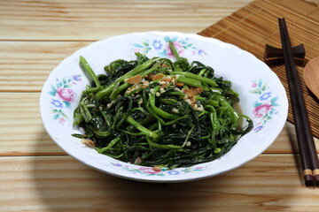 Fried and stirred fresh morning glory with garlic and seasoning with salt soya bean sauce on the plate. Famous traditional vegetarian menu in Asian restaurant. High fiber and vitamin food. 