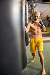 Serious gray-haired barefoot Caucasian sportsman practicing kickboxing