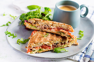 Grilled club sandwich panini with beef, tomato, cheese, lettuce and cup of coffee. Delicious breakfast or snack.