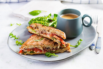 Grilled club sandwich panini with beef, tomato, cheese, lettuce and cup of coffee. Delicious breakfast or snack.