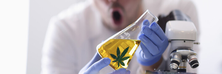 Man in goggles in rubber gloves holds flask with yellow liquid in chemical laboratory closeup....