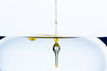 Detail of dash of olive oil drops gliding into glass of water isolated on white background