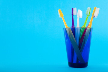 A group of colorful toothbrushes in a blue glass. Studio photo isolated on blue background. Selective focus on object. 