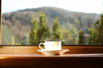 Saucer with cup of hot drink on wooden windowsill