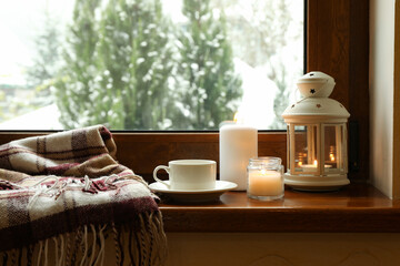 Plaid, cup, candles and lantern on wooden windowsill
