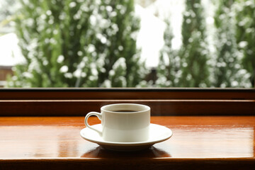 Saucer with cup on wooden windowsill against snowy weather background