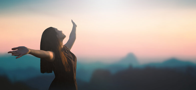 Celebration of life day concept: Happy Asian girl raised hand on blurred mountain sunrise background. Phang-nga, Thailand, Asia