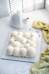 On a white plate, a teapot and a mousse cake with strawberry filling with a velvet white coating in the form of bubbles.