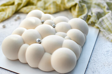 On a white plate a mousse cake with strawberry filling with a velvet white coating in the form of bubbles.